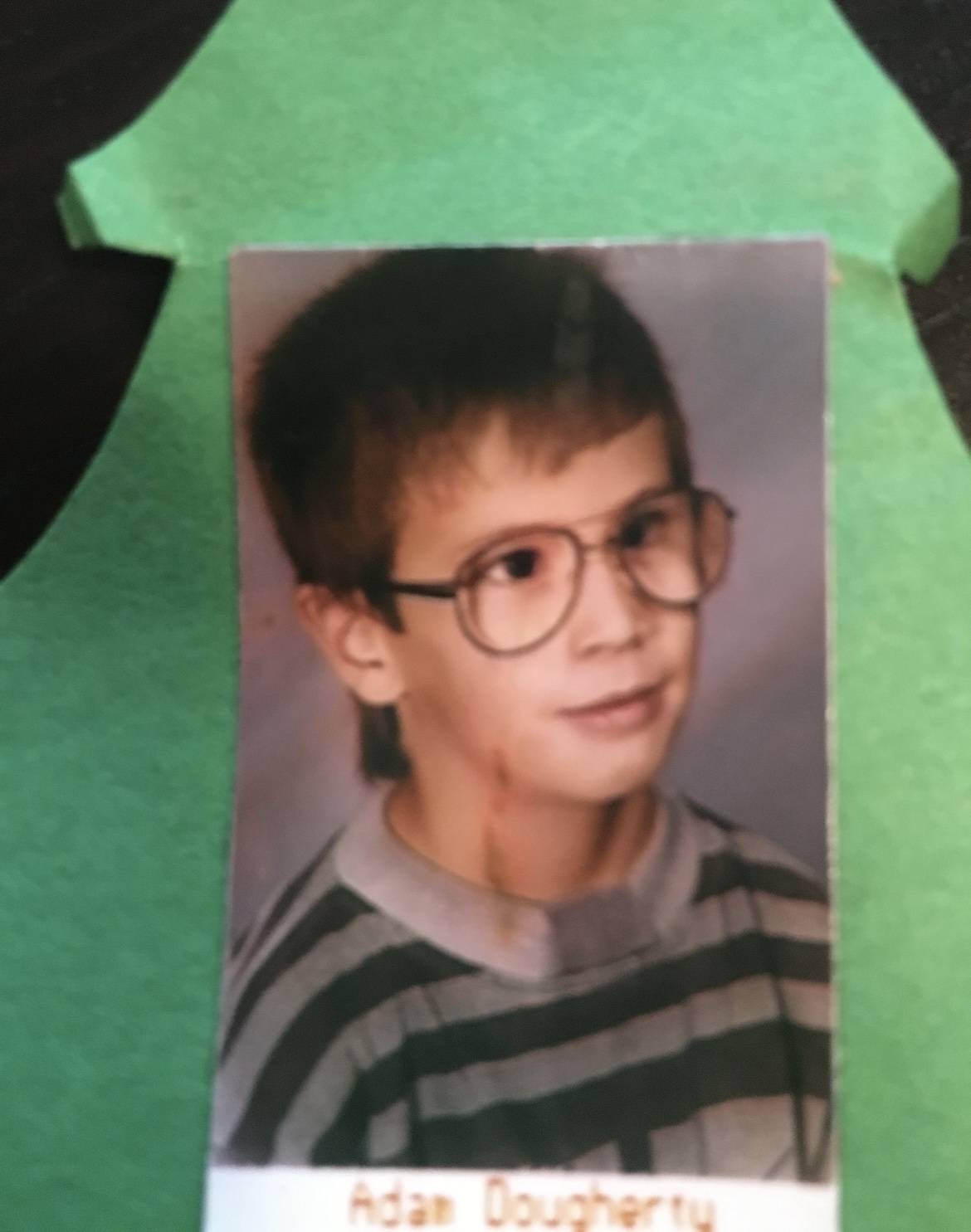 Adam's grade-school portrait, big glasses and a striped sweater, on green construction paper